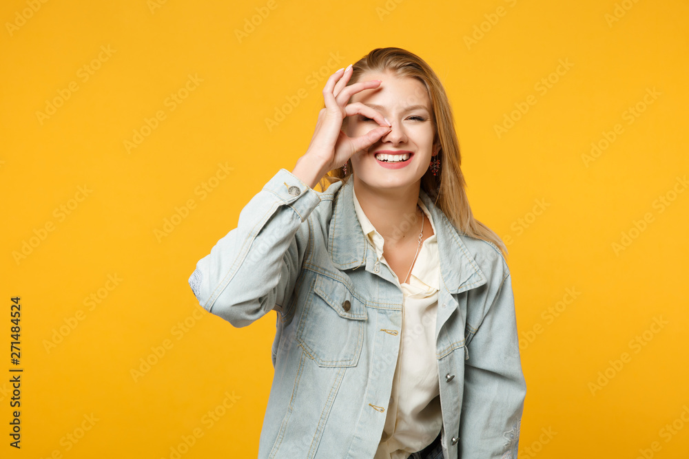 Laughing smiling young woman in denim casual clothes hold hands near eyes, imitating glasses or binoculars isolated on yellow orange background in studio. People lifestyle concept. Mock up copy space. Laughing smiling young woman in denim casual clothes hold hands near eyes, imitating glasses or binoculars isolated on yellow orange background in studio. People lifestyle concept. Mock up copy space.