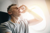 Man drinks water in an airplane before takeoff. Concept lays ears