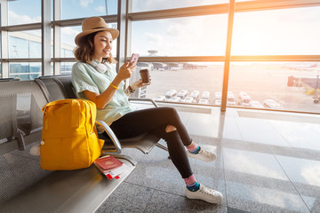 Happy asian woman waiting for her airplane in airport with passport and baggage. Vacation and journey concept