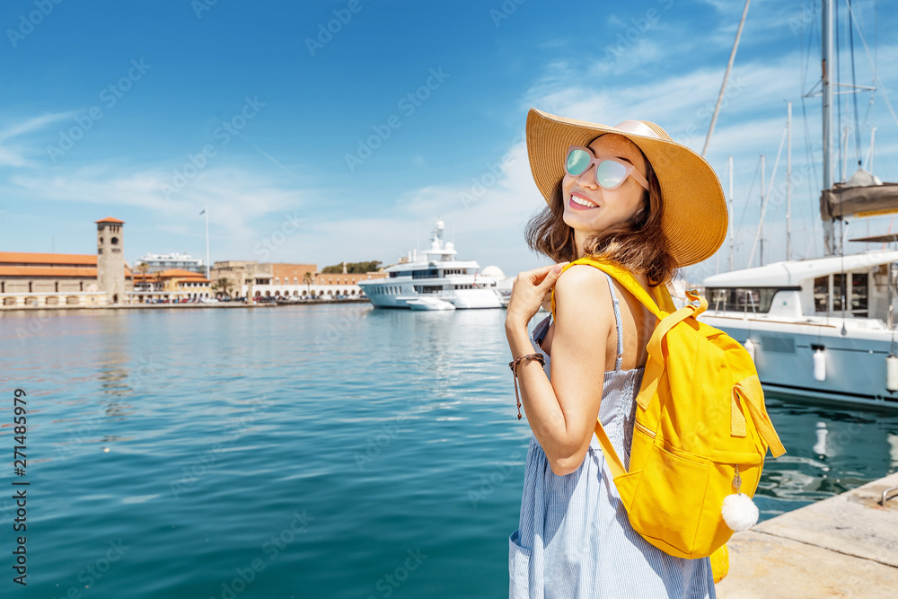 Asian girl traveler with big hat and backpack on vacation in the popular Greek island of Rhodes