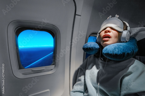 Asian girl sleeping in her seat on the plane near the window in a mask and with a pillow to sleep. The concept of travel with comfort and jetlag