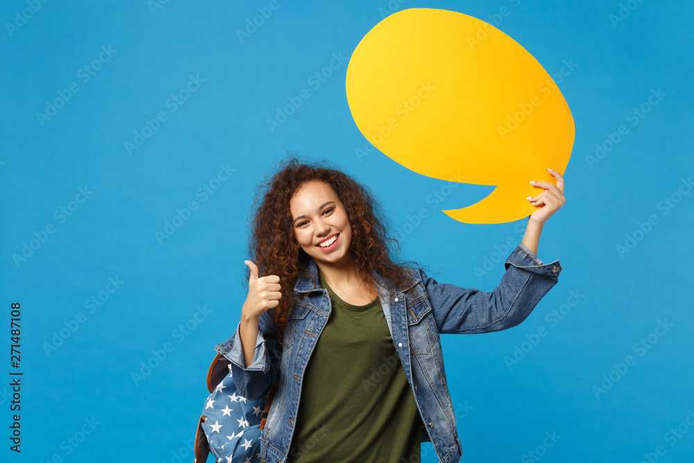 Young african american girl teen student in denim clothes, backpack hold say cloud isolated on blue background studio portrait. Education in high school university college concept. Mock up copy space. Young african american girl teen student in denim clothes, backpack hold say cloud isolated on blue background studio portrait. Education in high school university college concept. Mock up copy space.