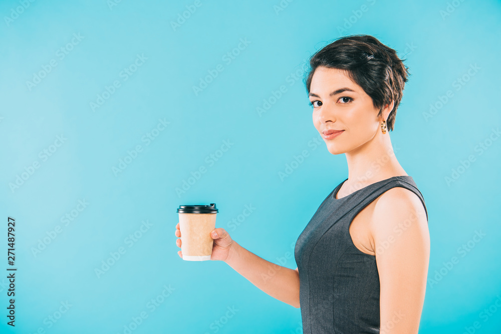 pretty mixed race woman holding paper cup while looking at camera on blue background pretty mixed race woman holding paper cup while looking at camera on blue background