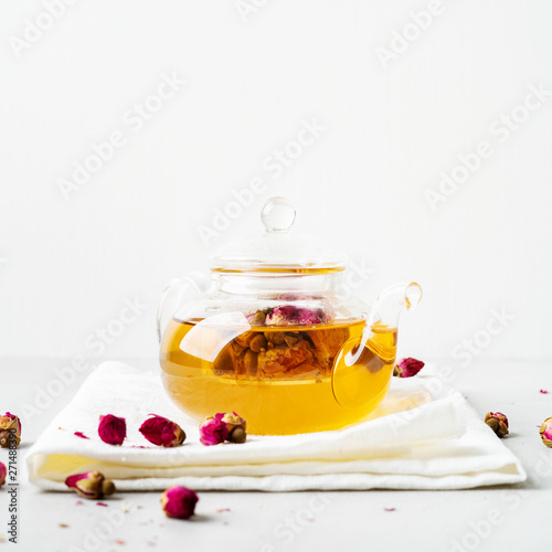 Herbal tea with dried pink flower roses buds in transparent teapot over gray background with copy space. Brewing and Drinking tea.