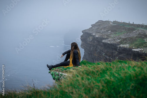 Woman sitting on the cliff's edge at Cliffs of Moher