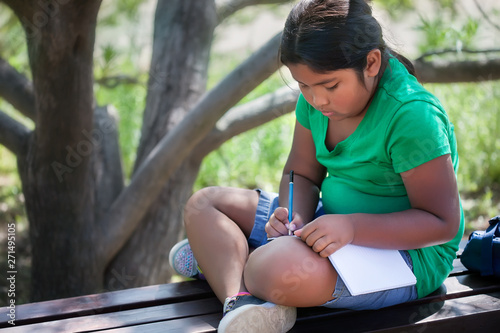 A homeschooled child sitting in an outdoor garden in a relaxed pose, while solving or learning elementary school level subjects.