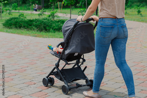 Beautiful woman with a child in a pram walks through a summer park.