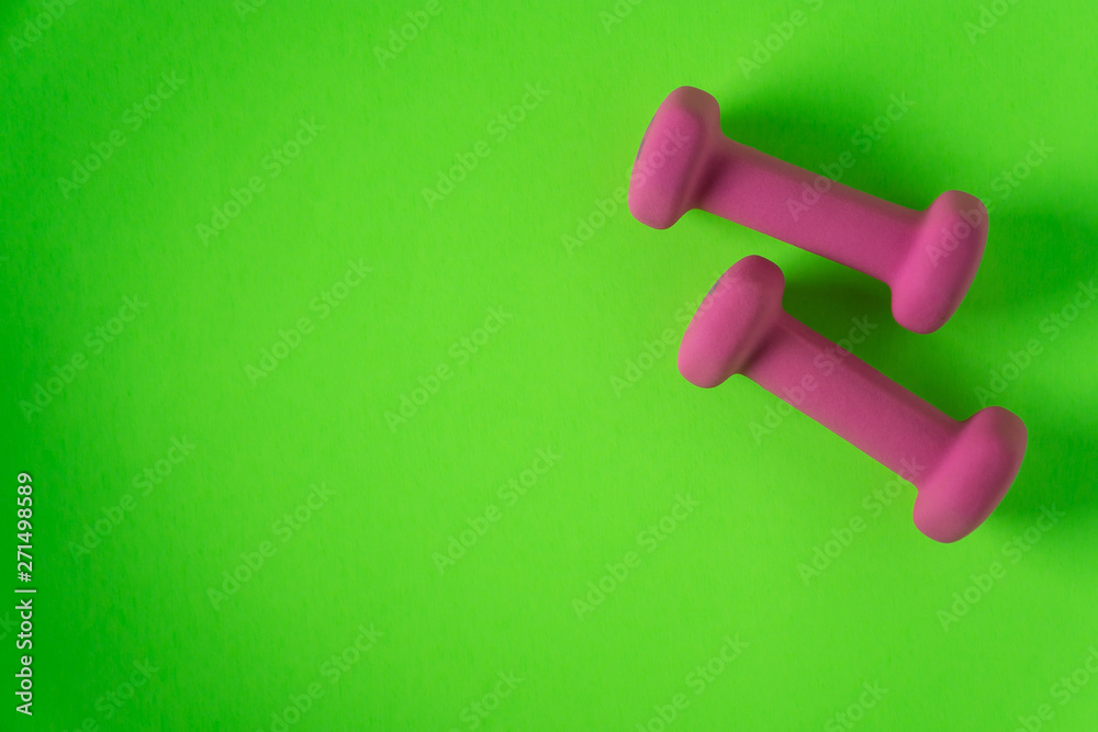 Fitness equipment with womens pink weights/ dumbbells isolated on a lime green background with copyspace Fitness equipment with womens pink weights/ dumbbells isolated on a lime green background with copyspace