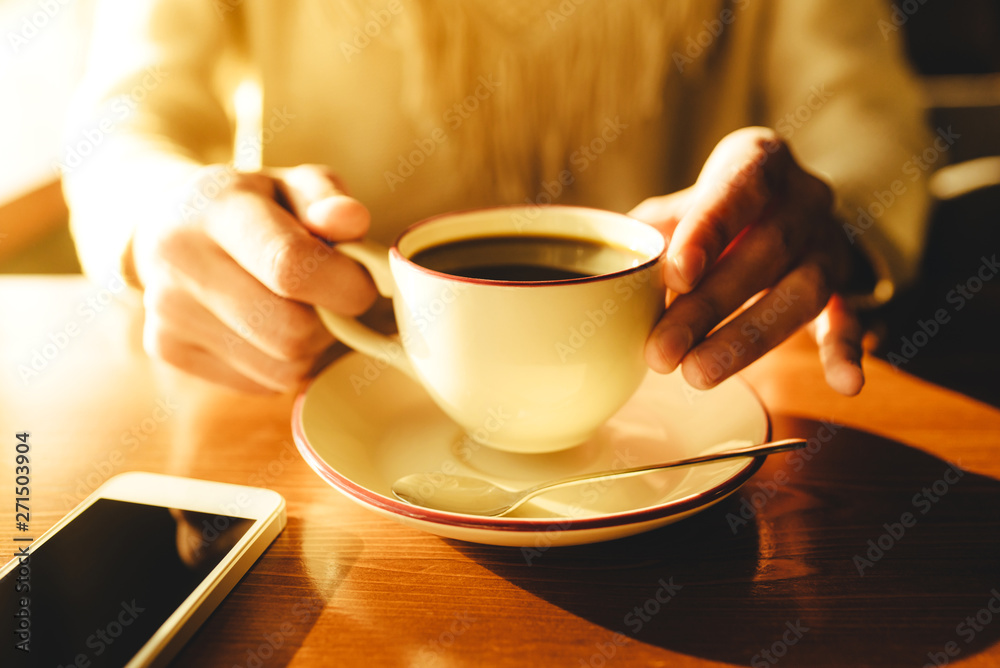 Woman holding in hands cup of coffee on wooden table in cafe