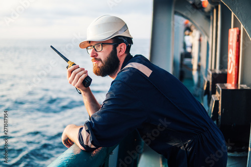 Deck Officer on deck of offshore vessel or ship , wearing PPE personal protective equipment. He holds VHF walkie-talkie radio in hands. Dream work at sea photo