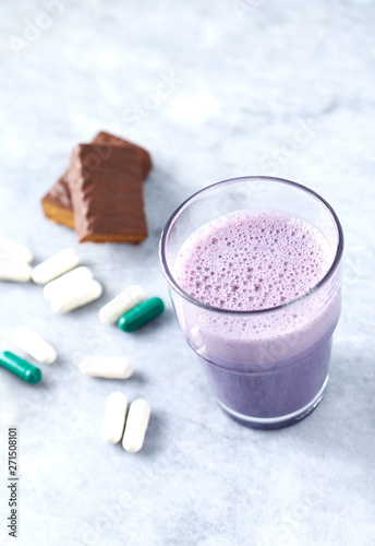 Protein bar in two pieces, Glass of Protein Shake with Milk and Blueberries, L-Carnitine and Beta-alanine capsules in background. Concept for Sport nutrition. Copy space. 