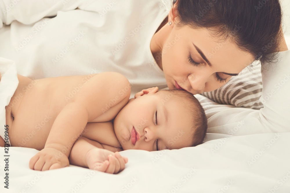 Mother kissing her sleeping newborn baby in bed Mother kissing her sleeping newborn baby in bed