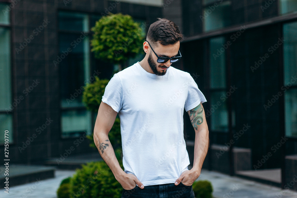 A young stylish man with a beard in a white T-shirt and glasses. Street photo A young stylish man with a beard in a white T-shirt and glasses. Street photo
