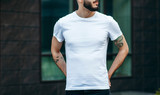 A young stylish man with a beard in a white T-shirt and glasses. Street photo