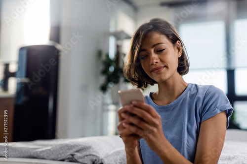 Young smiling woman text messaging in mobile phone in the bedroom.