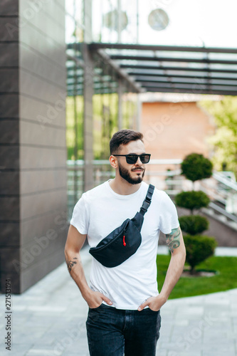 Stylish bearded hipster in the at the city in a white T-shirt with waist bag