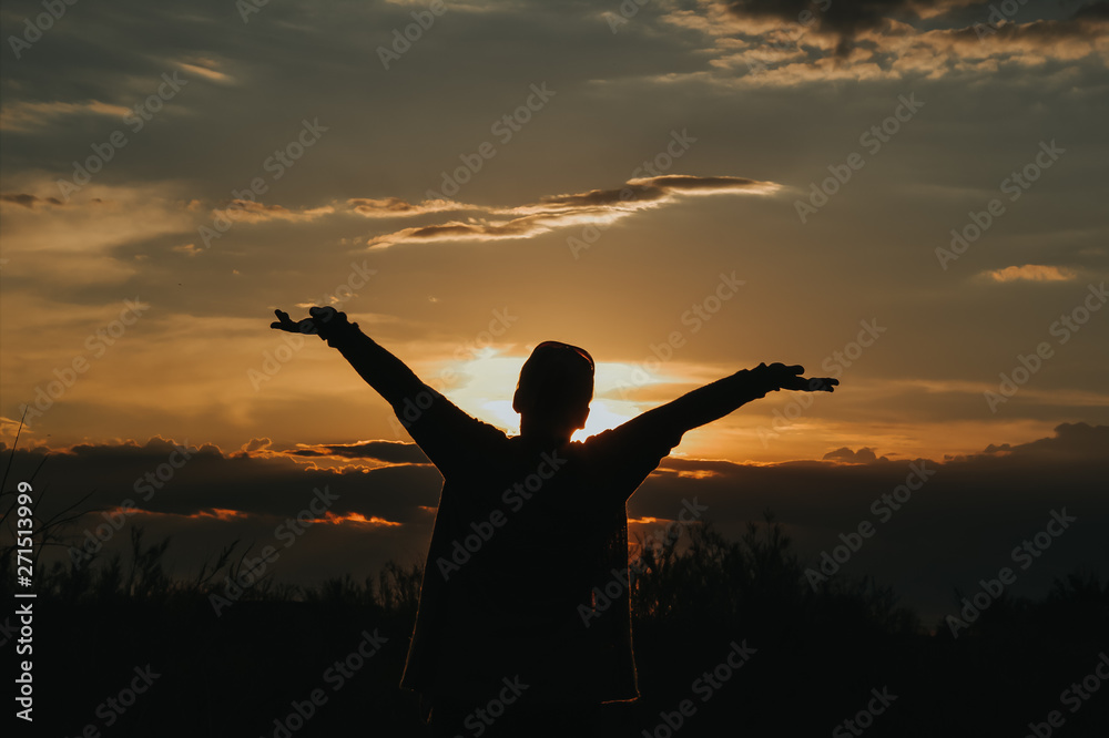 silhouette of a woman with arms outstretched at sunset with sky in the background. 
