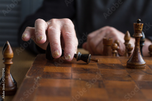 The hand of an old man puts a black king's figure on the board acknowledging loss, concept business games, selective focus