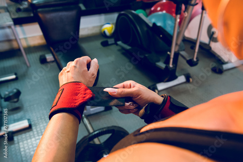Close up on female hands with long nails putting wrap bandages on her wrists for powerlifting body building training sport equipment at the gym