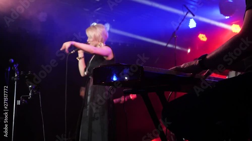 Female singer performs on the stage on the background. Keyboardist on the foreground. Slow motion