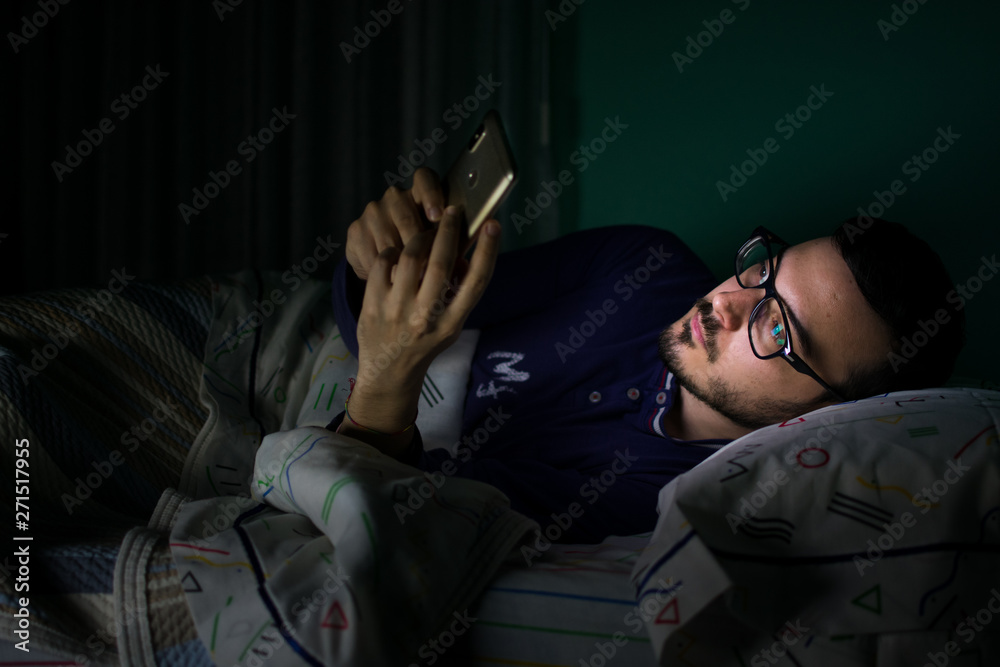 Fototapeta premium Man looking his mobile phone in the bed at night