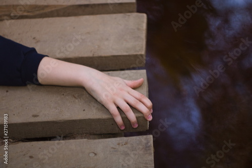 Children's hand clings to the edge of a wooden hinged bridge over the river