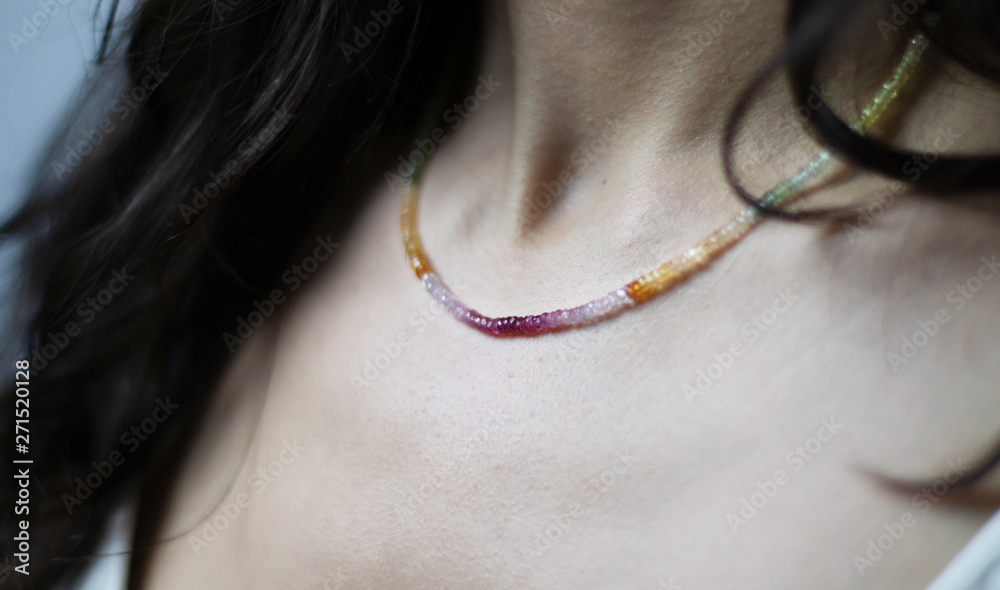 Necklace of multicolored and shiny stones on the neck of a young woman.