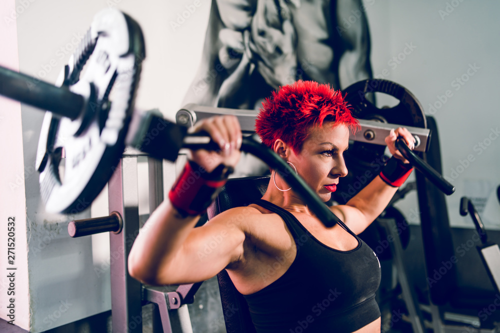 Fototapeta premium Young muscular woman female athlete bodybuilding at the gym training shoulder press machine fitness weight loss