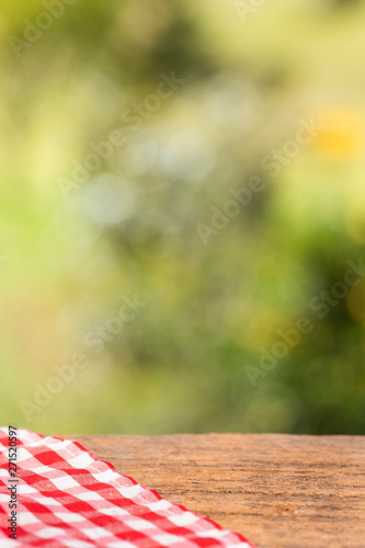 Checkered red napkin on wooden table against green blurred background.