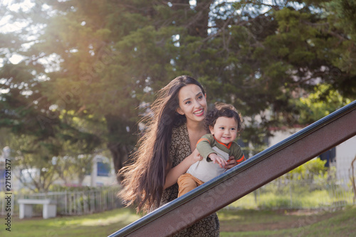 Mom having fun with her 2 year old son on the outdoor park slide on a beautiful sunny afternoon photo