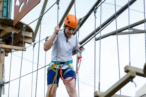 Happy child, healthy teenager school boy in orange helmet enjoys activity in a climbing adventure rope park on a sunny summer day 