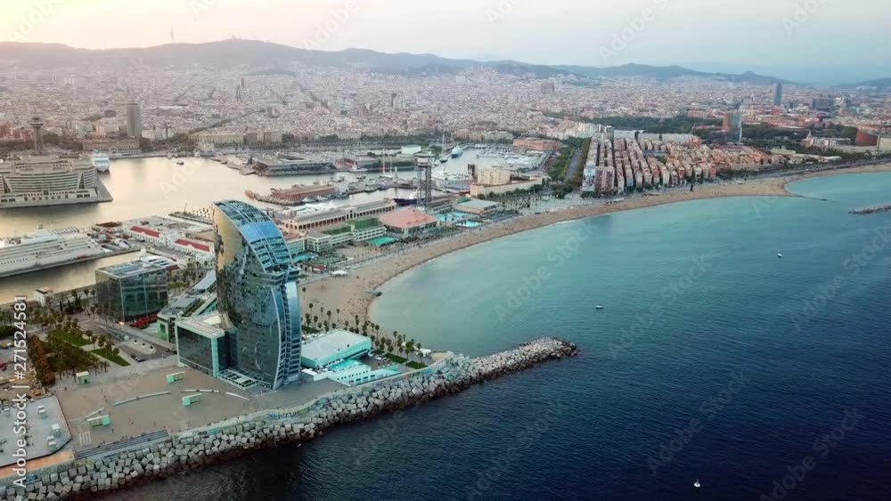 Aerial, reverse, drone shot, overlooking the barcelonica beach, hotels and the coast of the city, at sunset, on a sunny summer evening, in Barcelona, Spain