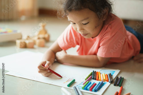 Картината върху платно Cute little asian girl drawing homework and writing with color Wax crayons on pa