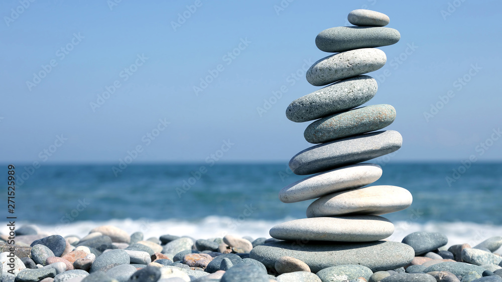 folded pyramid of smooth stones on the seashore. - obrazy, fototapety, plakaty 