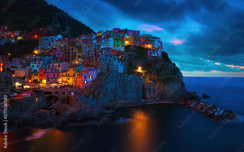 night view of cliffside town of manarola next to the Ligurian sea with horizon and sunset sky.