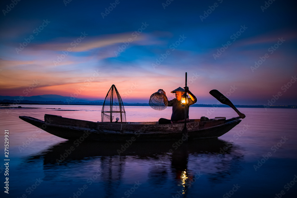 Traditional asia fisherman with using a bamboo square dip net on wooden boat at beautiful morning Lake.