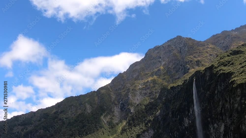 Time lapse of mountains with a large waterfall falling down a cliff. Moving clouds and a blue sky. static, wide angle