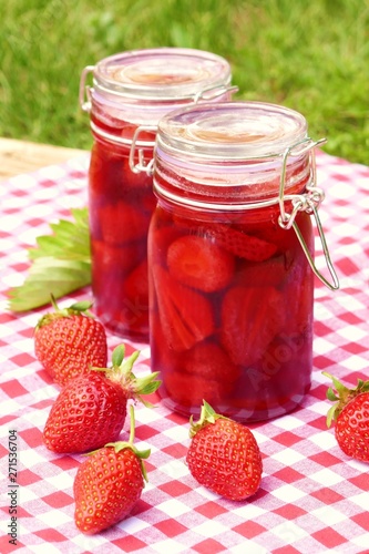 Strawberry jam in glass jars set and fresh strawberries on a wooden table with a red checkered napkin on a green vegetable background.Homemade jam. Canned berries. Healthy vegetarian 