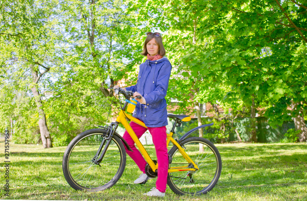 Young girl standing with a bicycle in a city park on a clear sunny day