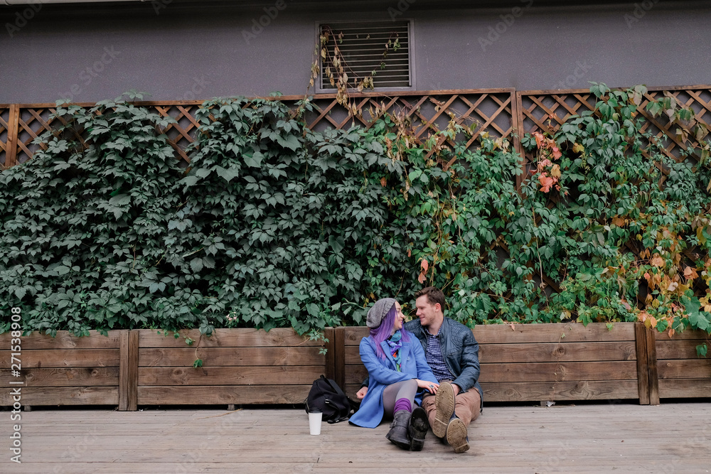 Couple is sitting in an embrace on a wooden floor on the street. Woman and man smile. Couple is sitting in an embrace on a wooden floor on the street. Woman and man smile.