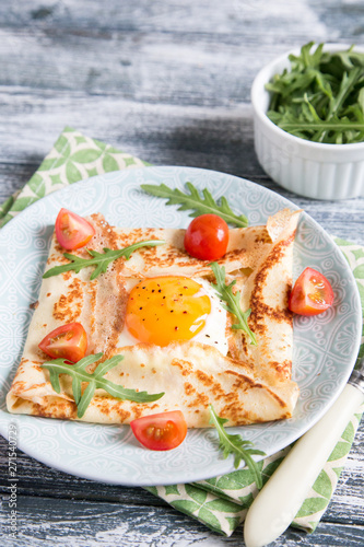 Crepes with eggs, cheese, arugula leaves and tomatoes. Galette complete. Traditional dish galette sarrasin.