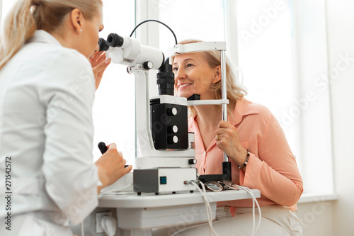 Smiling good-looking senior lady sitting in front of professional oculist
