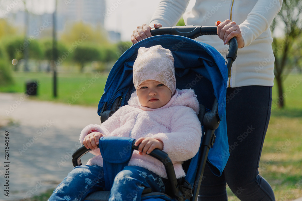 Young mother with a baby in a stroller in a summer park. Young mother with a baby in a stroller in a summer park.