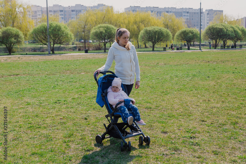 Young mother with a baby in a stroller in a summer park. Young mother with a baby in a stroller in a summer park.