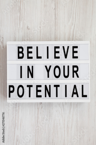 'Believe in your potential' words on a modern board on a white wooden background, top view. Flat lay, overhead, from above. Close-up.