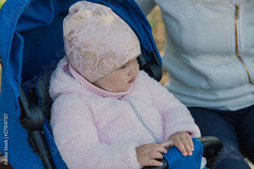 A young mother with a baby in a pram sits on a bench on a sunny day.