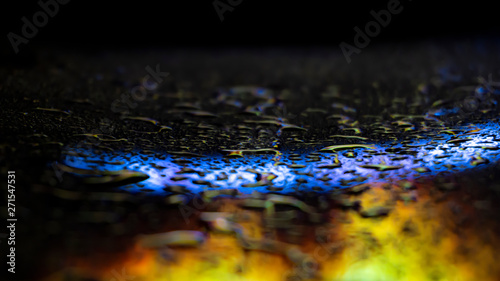 Dark background. Spilled liquid on the mirror surface, the reflection of neon lights, glare, blurred bokeh background. Neon, night view of the streets of a big city.
