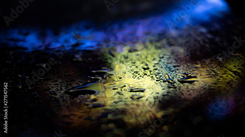 Dark background. Spilled liquid on the mirror surface, the reflection of neon lights, glare, blurred bokeh background. Neon, night view of the streets of a big city.