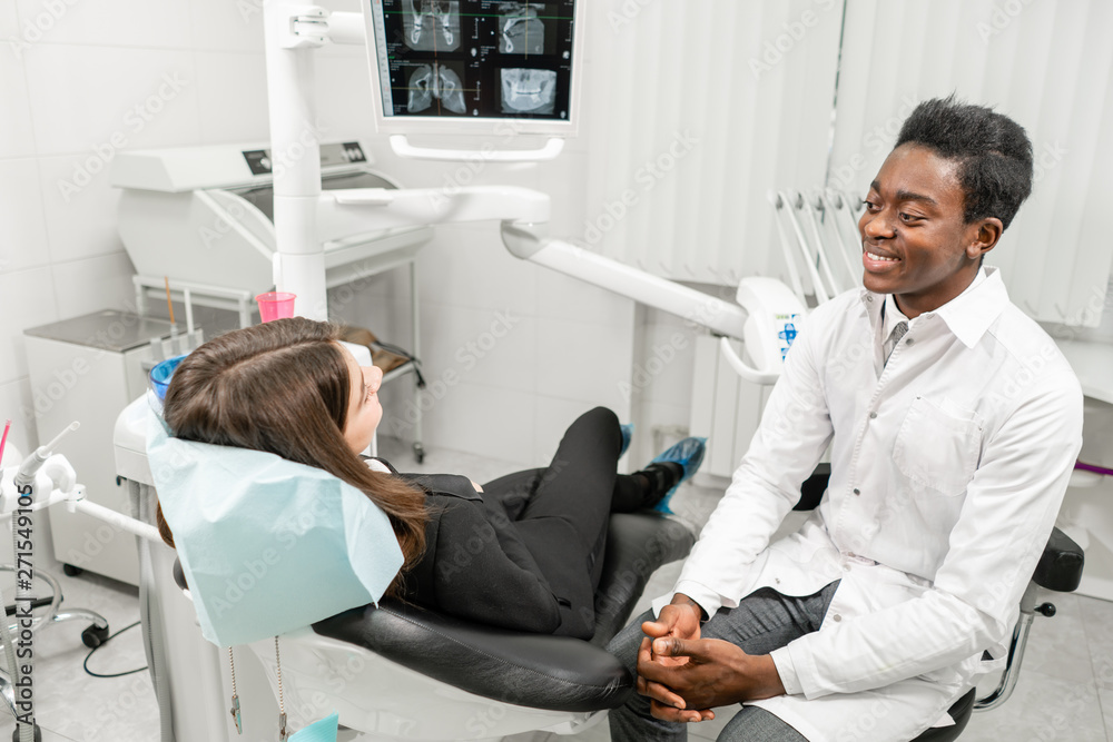 Obraz premium Young African male dentist with a patient. Woman in the dentist chair at dental clinic. Medicine, health, stomatology concept. dentist treating a patient.