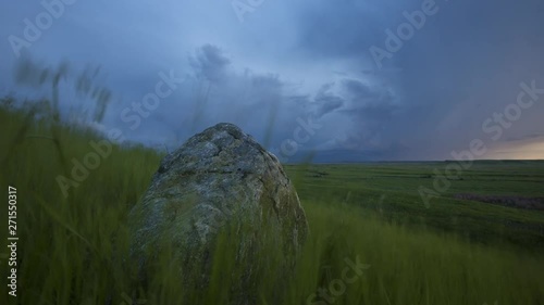Storm clouds move over a green field at dusk creating a dark atmosphere